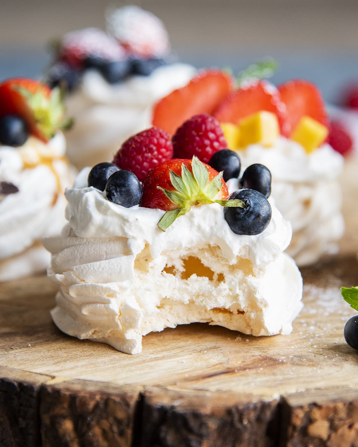 A mini pavlova with a bite out of it showing the marshmallowey middle. It is topped with fresh berries.