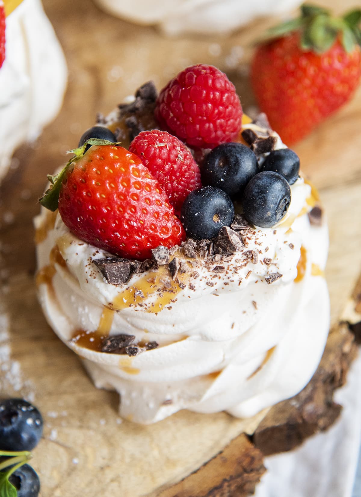 A close up of a mini pavlova topped with strawberries , blueberries, raspberries, and chocolate shavings.