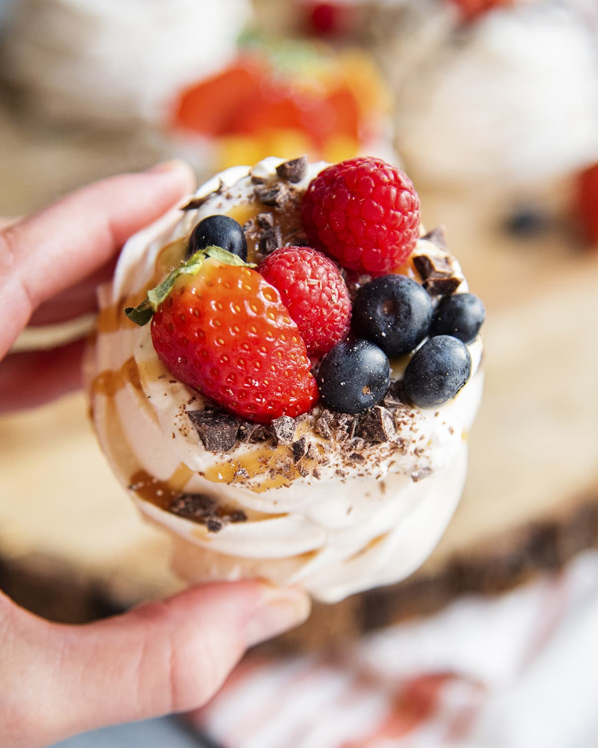 A hand holding a mini pavlova topped with caramel strup and fresh berries.