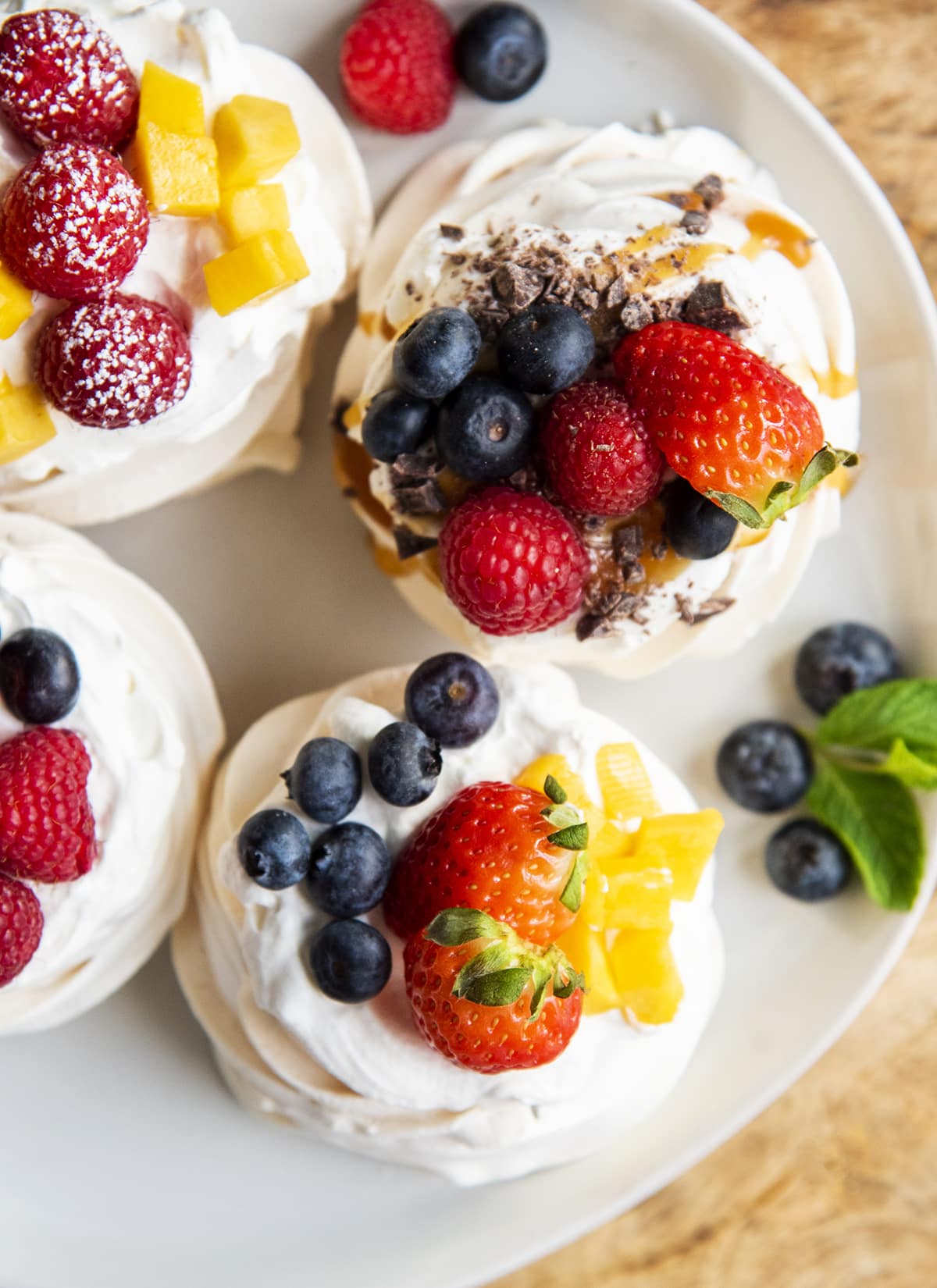 An overhead photo of a plate of mini pavlovas topped with strawberries, blueberries, mango, and more.