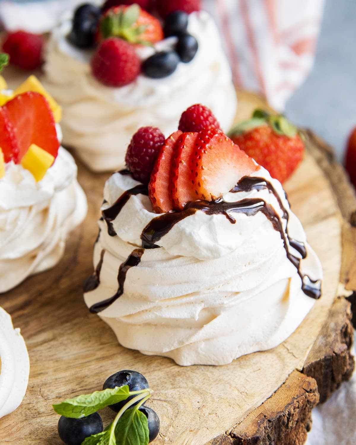 A small pavlova on a board topped with chocolate syrup and strawberries.