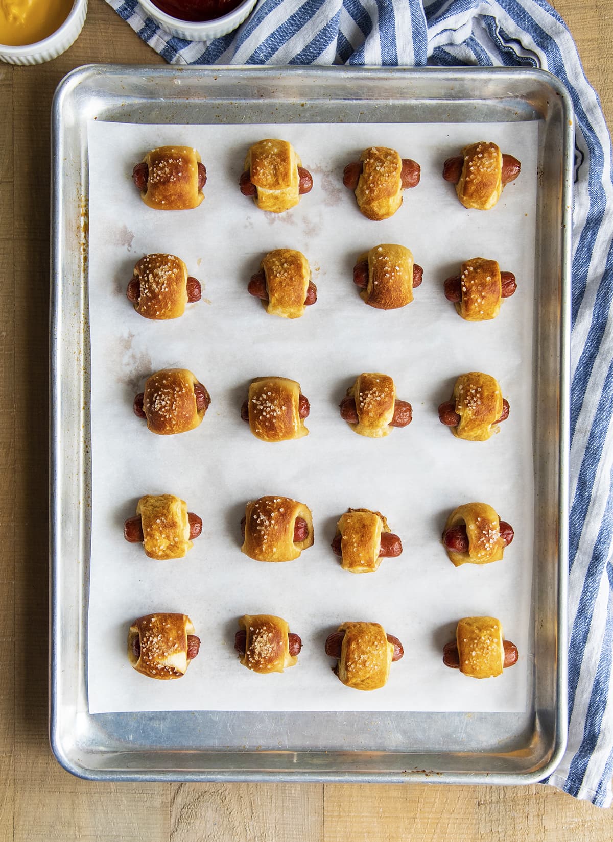 An overhead photo of pretzel pigs in a blanket in rows on a cookie sheet.