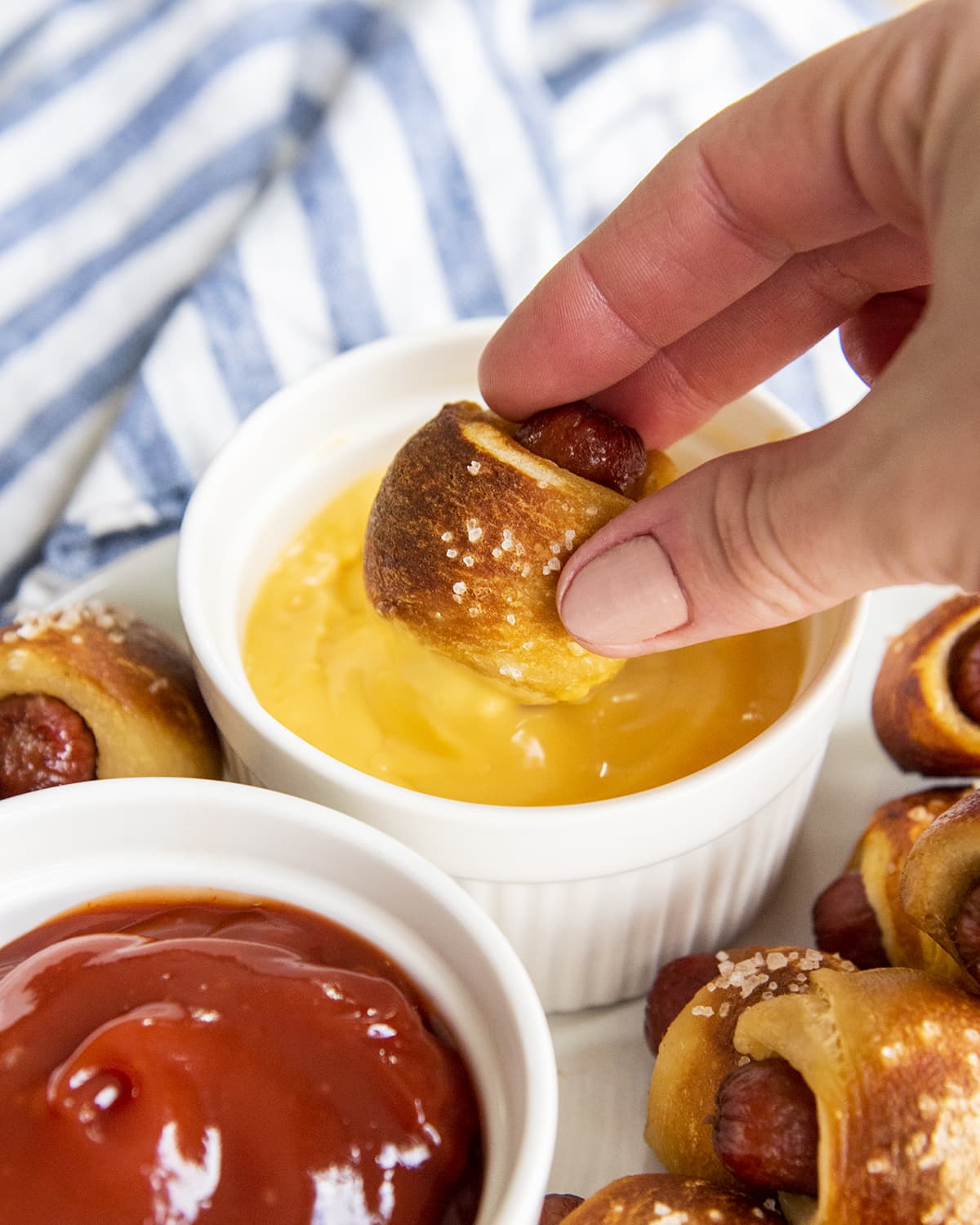A hand holding a pretzel pigs in a blanket dipping into a bowl of nacho cheese sauce.