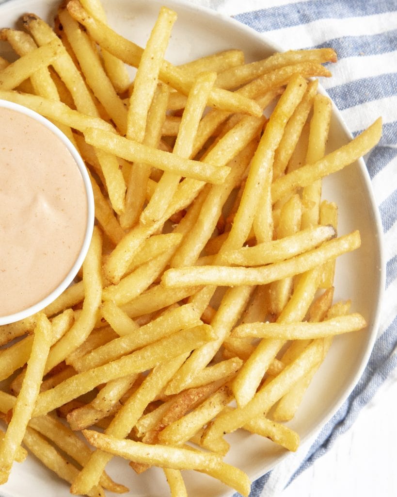 A plate of french fries with a bowl of dip on the side.