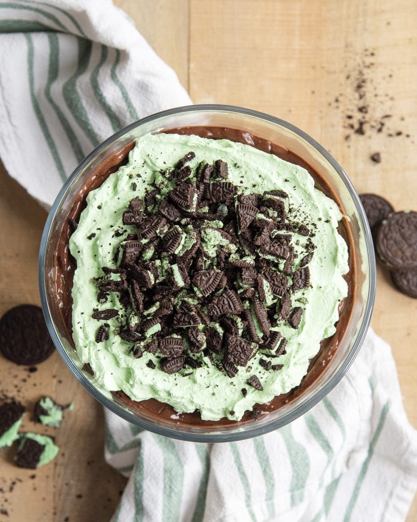 An overhead photo of a chocolate and mint trifle topped with mint Oreo pieces in a large trifle bowl.