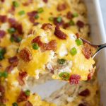 A scoop of crack chicken casserole topped with bacon bits and green onions.