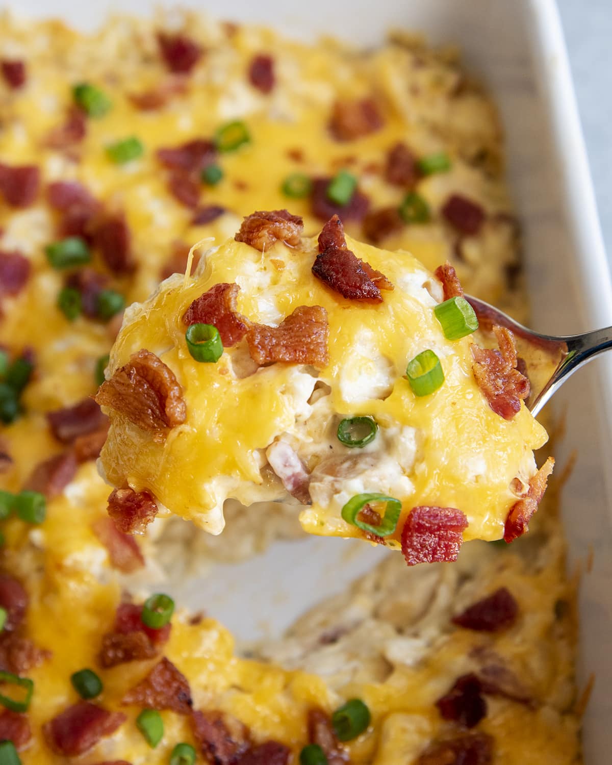 A scoop of crack chicken casserole topped with bacon bits and green onions.
