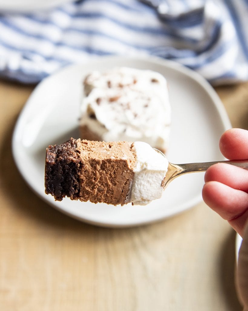 A bite of chocolate mousse on a brownie, topped with whipped cream on a fork.