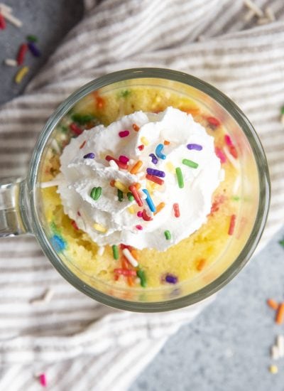 An overhead photo of a funfetti mug cake topped with a dollop of whipped cream and more sprinkles.