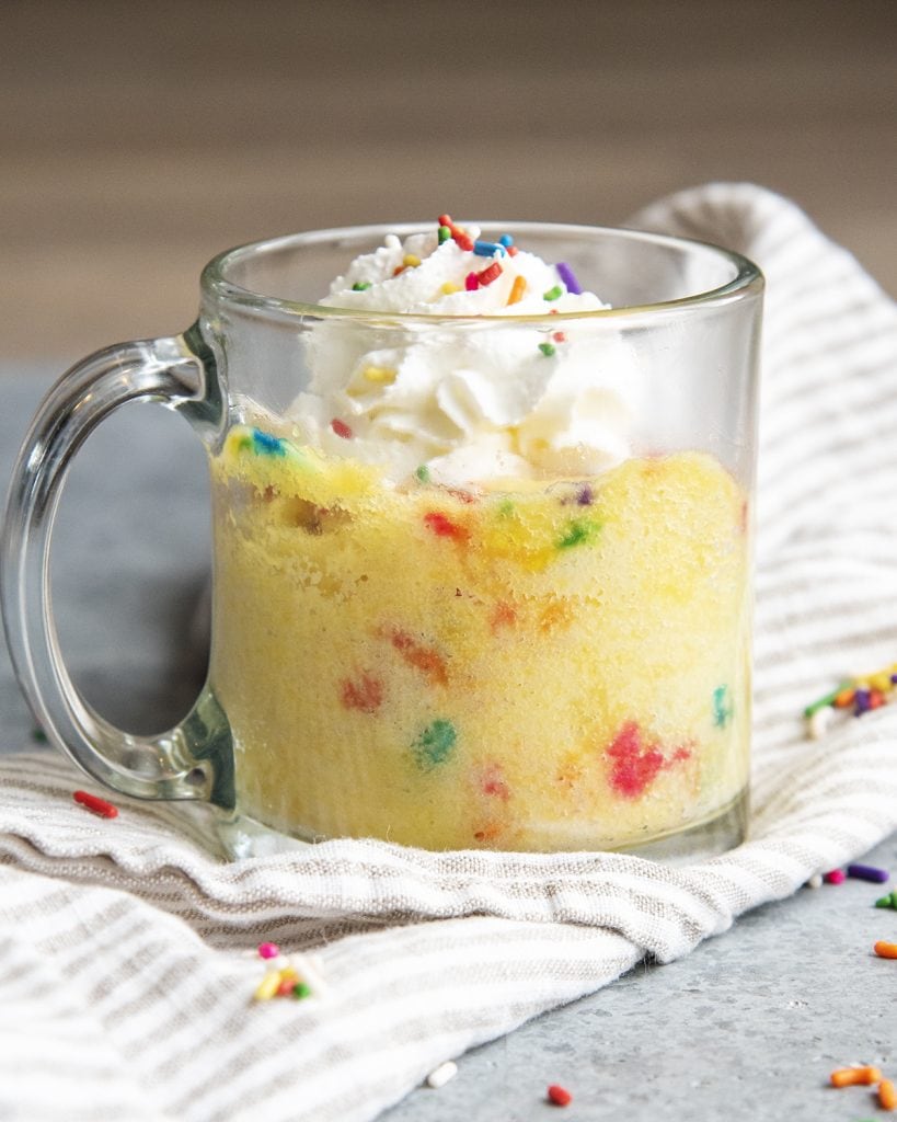 A side view of a funfetti mug cake topped with whipped cream and more sprinkles.