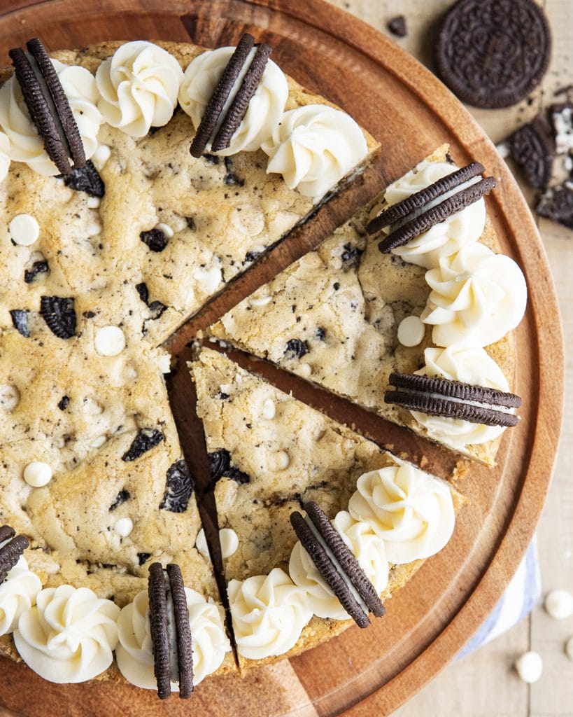 An overhead photo of a cookies and cream cookie cake filled with white chocolate chips and Oreo pieces topped with frosting.