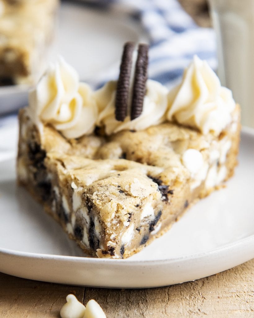 A close up of a piece of an Oreo filled cookie cake topped with buttercream on a plate.