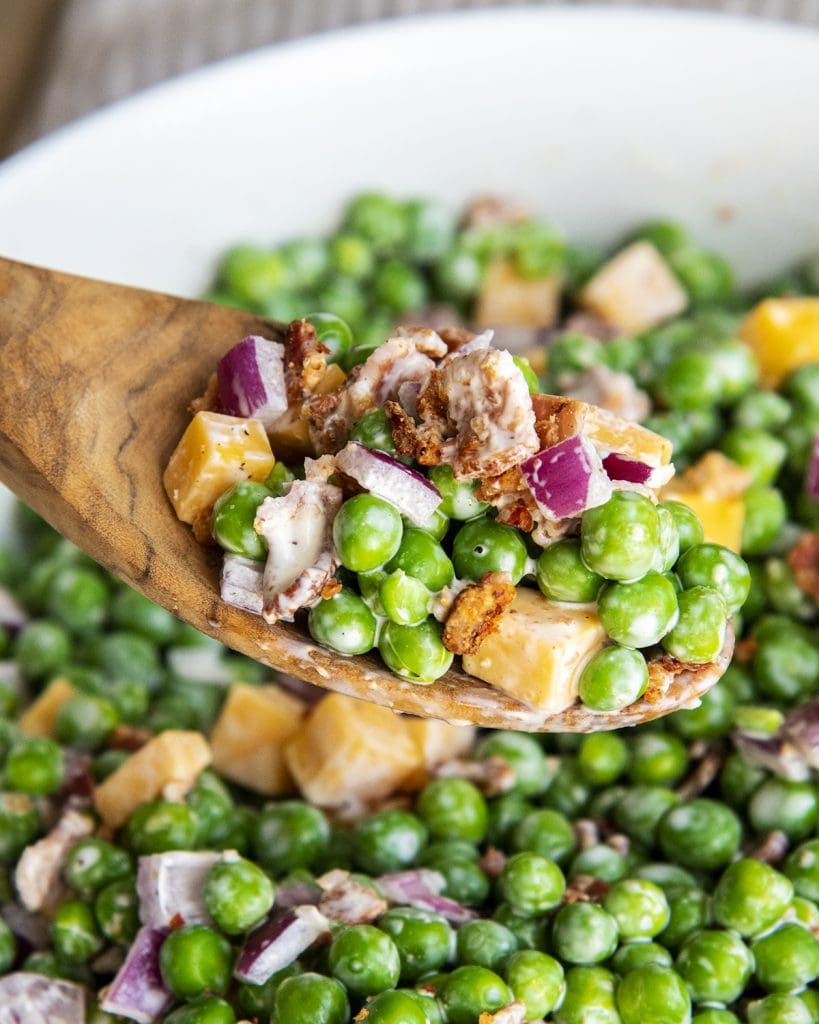 A spoonful of bacon pea salad above a bowl of it.