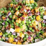 A bowl of creamy pea salad with cheddar cheese, bacon, and red onion.