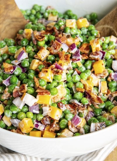 A bowl of creamy pea salad with cheddar cheese, bacon, and red onion.