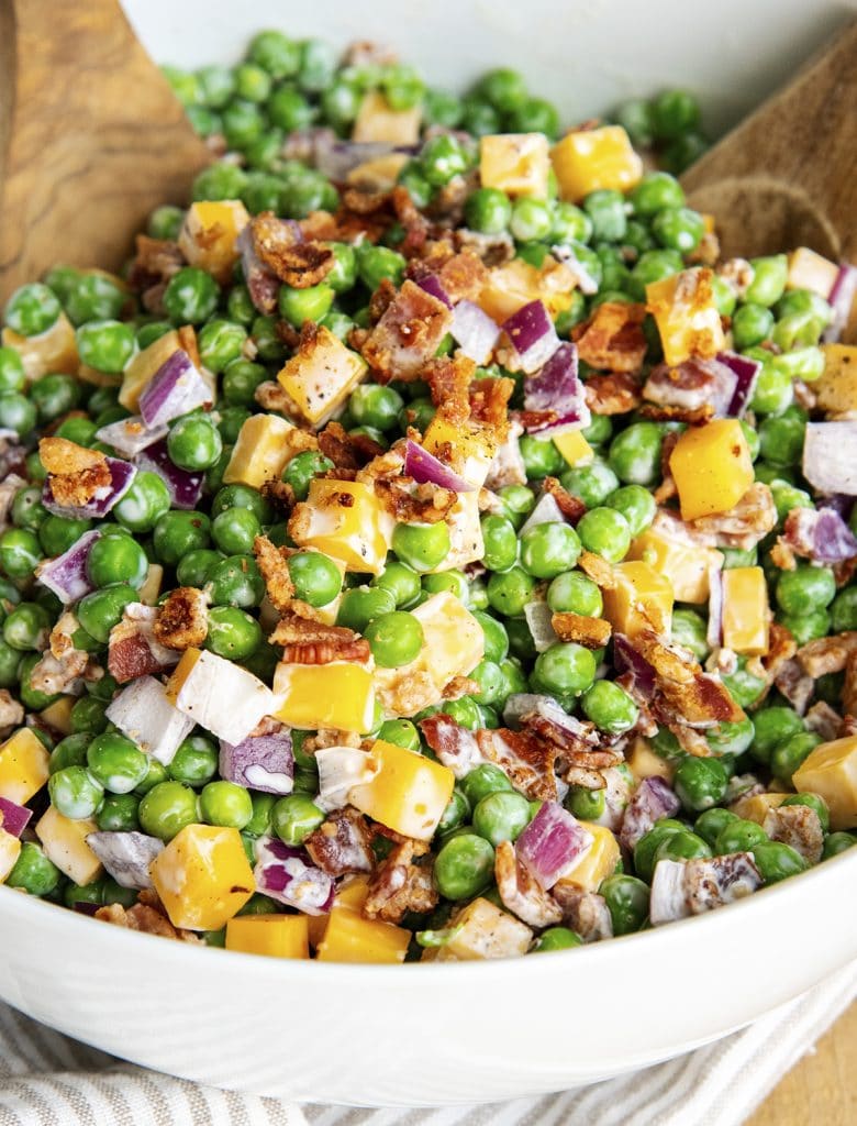 A bowl of creamy pea salad with cheddar cheese, bacon, and red onion.