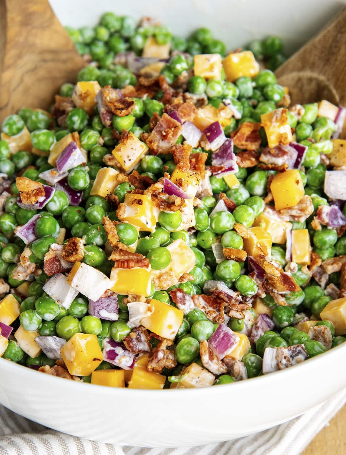 A bowl of creamy pea salad with cheddar cheese, bacon, and red onion.