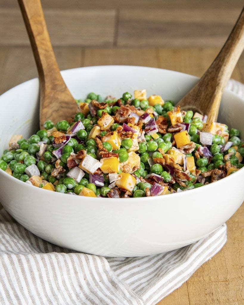 A bowl of bacon pea salad with two wooden spoons in the bowl.