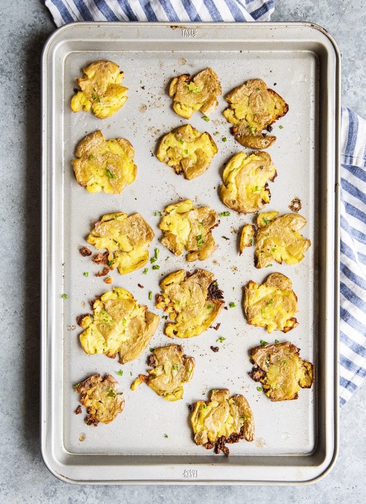 A pan of crispy smashed potatoes with fresh parsley sprinkled on top.