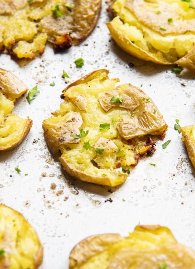 A close up of a smashed potato with crispy skins and topped with salt and pepper and parsley.
