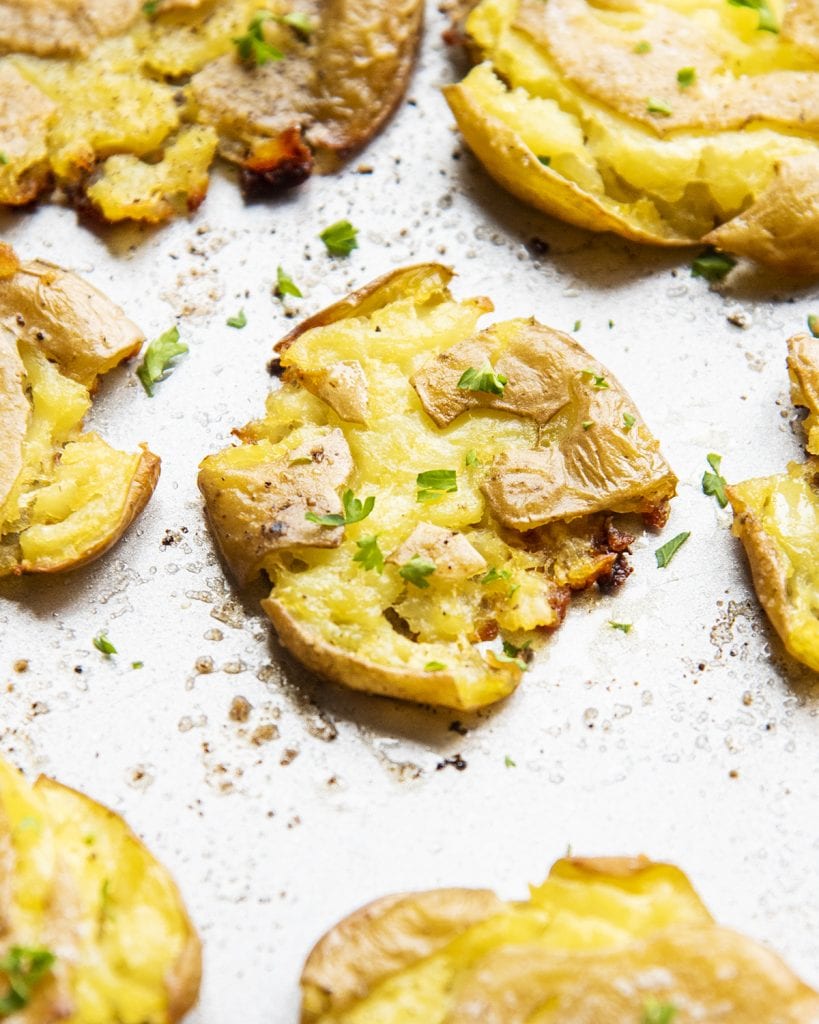 A close up of a smashed potato with crispy skins and topped with salt and pepper and parsley.