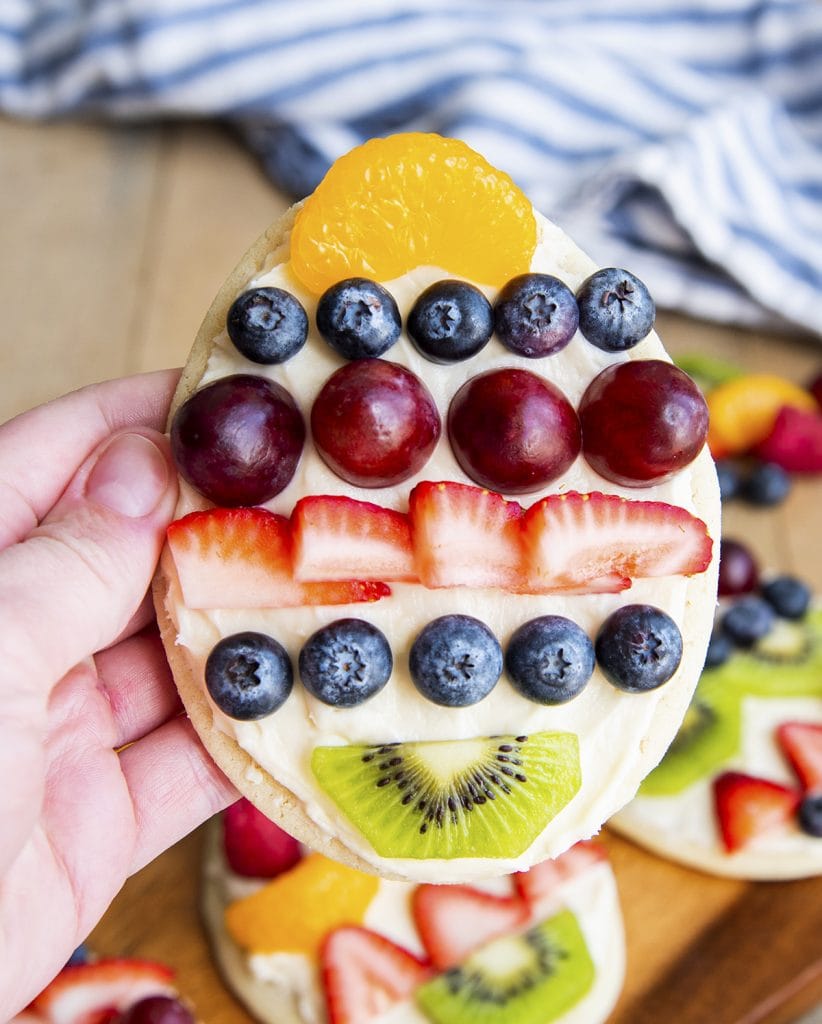 A hand holding an Easter Egg fruit pizza cookie topped with fresh fruit.