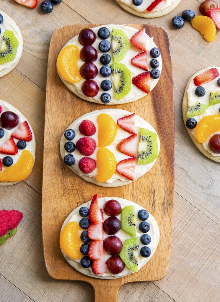 Three Easter egg fruit pizzas decorated with fresh fruit, and laying on a wooden board.