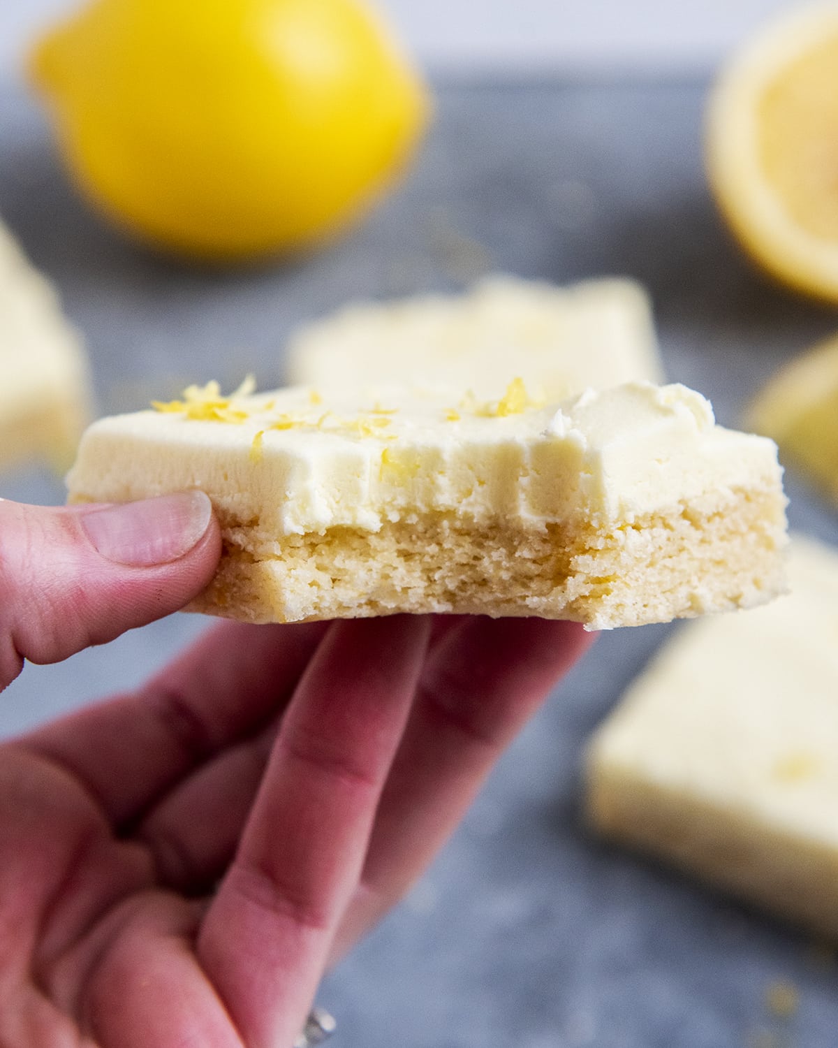 A hand holding a lemon sugar cookie bar with a bite out of it.