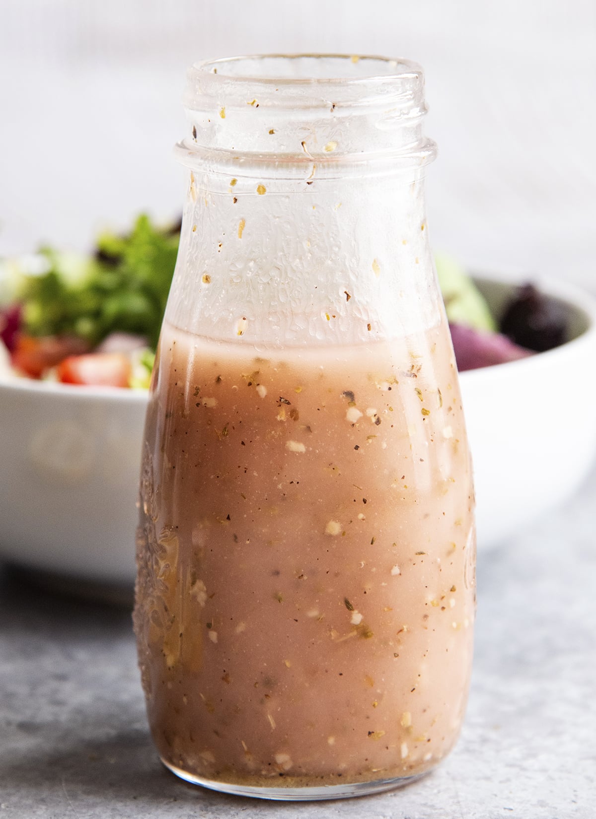 A close up of a bottle of red wine vinaigrette dressing in front of a bowl of salad.