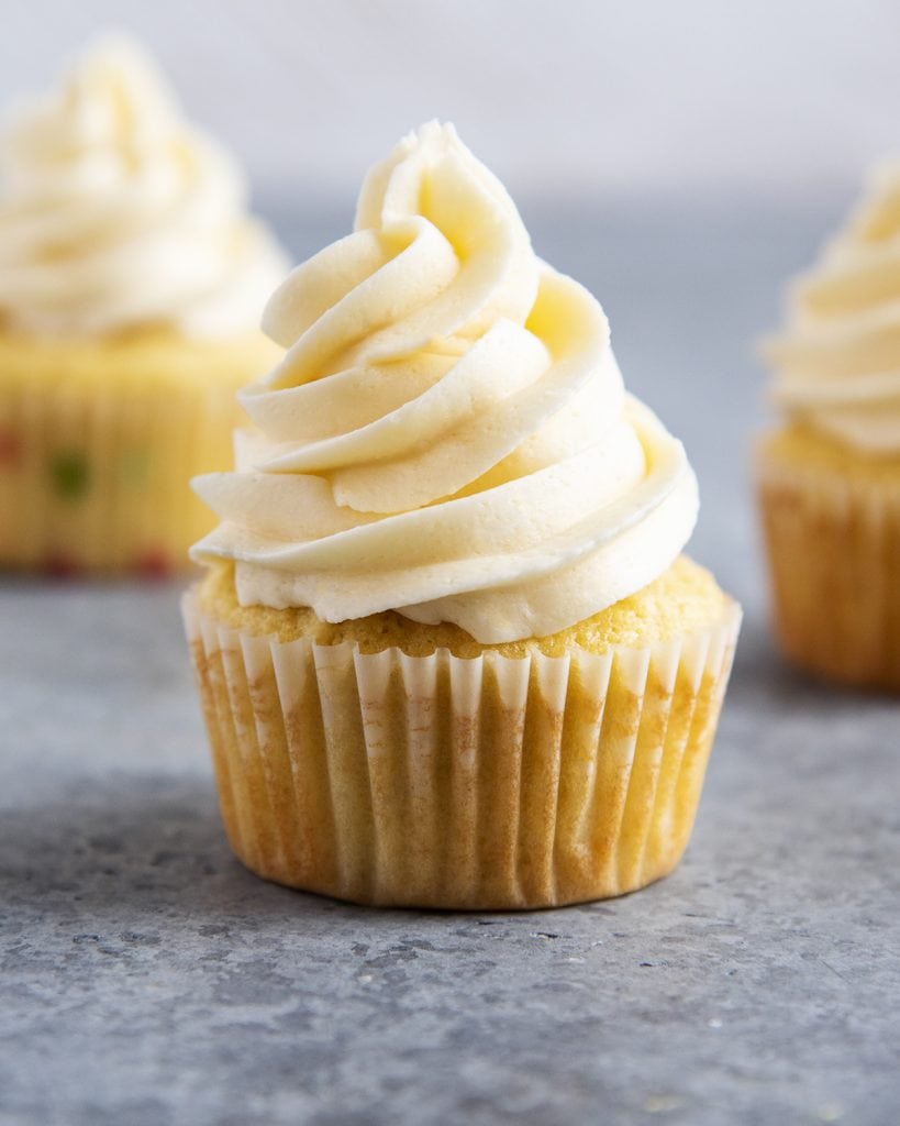 A vanilla cupcake topped with a vanilla buttercream frosting on a gray counter top.