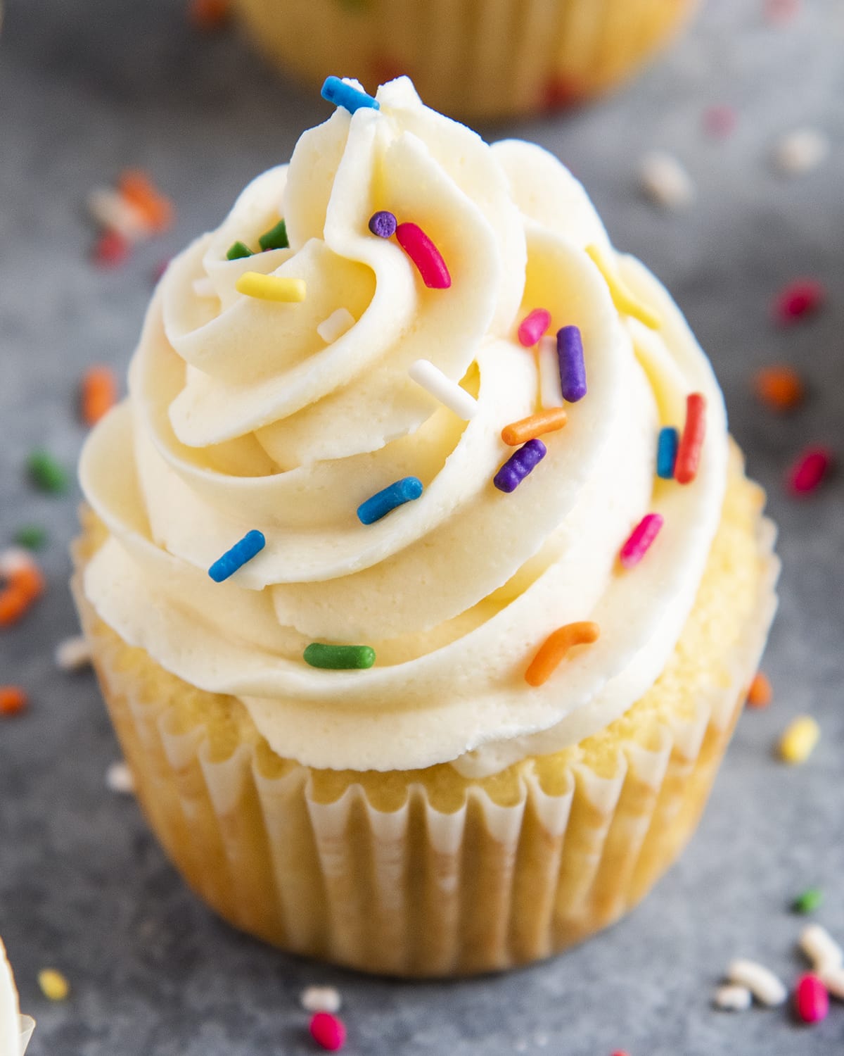 A close up of buttercream frosting topped with sprinkles on a cupcake.