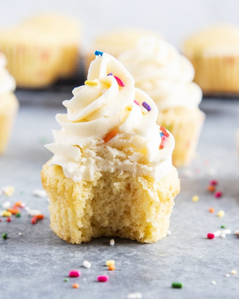 A frosted vanilla cupcake with a bite out of it.