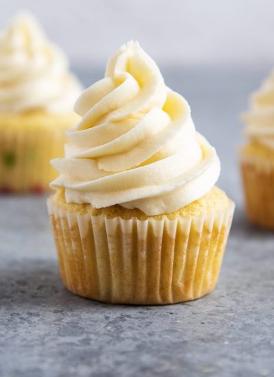 A vanilla cupcake topped with a vanilla buttercream frosting on a gray counter top.