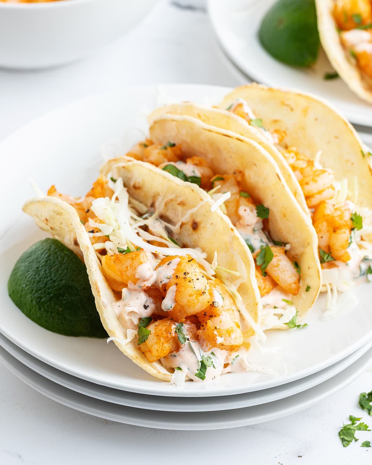 A plate of shrimp tacos topped with slaw and cilantro lime yogurt sauce.