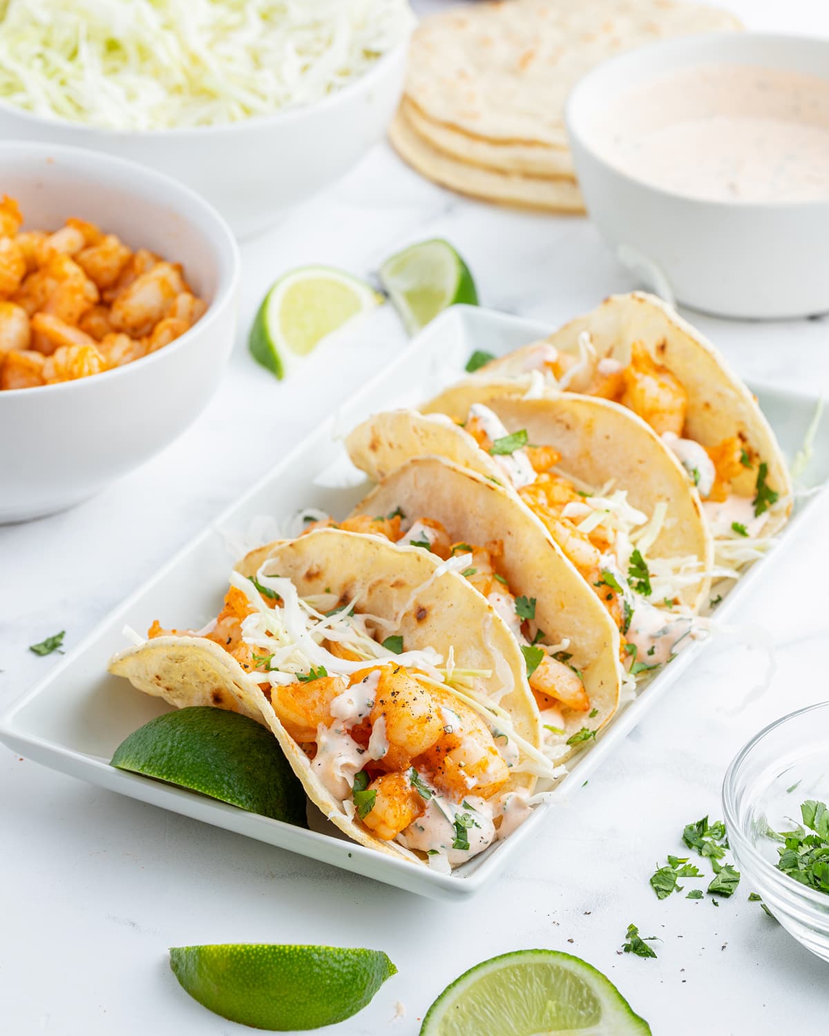 Shrimp tacos lined up on a plate with cabbage and cilantro on top.