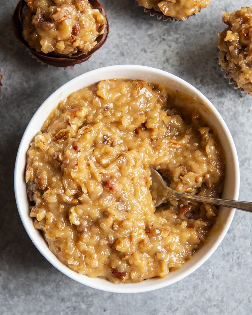 An overhead photo of a bowl of coconut pecan frosting with a spoon in it.