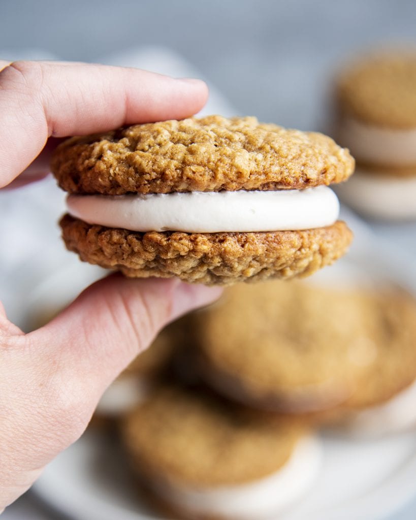 A hand holding a homemade oatmeal cream pie with marshmallow fluff frosting.