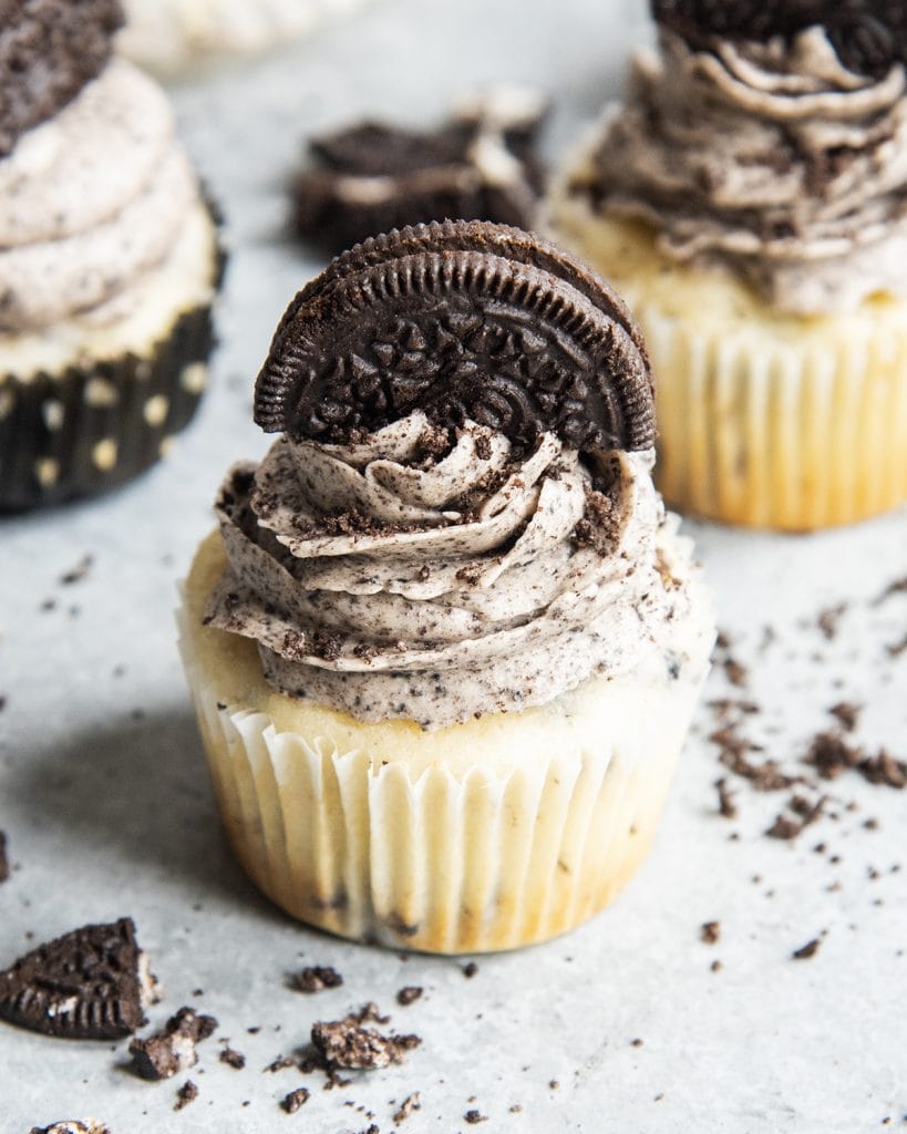 A vanilla Oreo cupcake topped with Oreo frosting and half an Oreo on top.