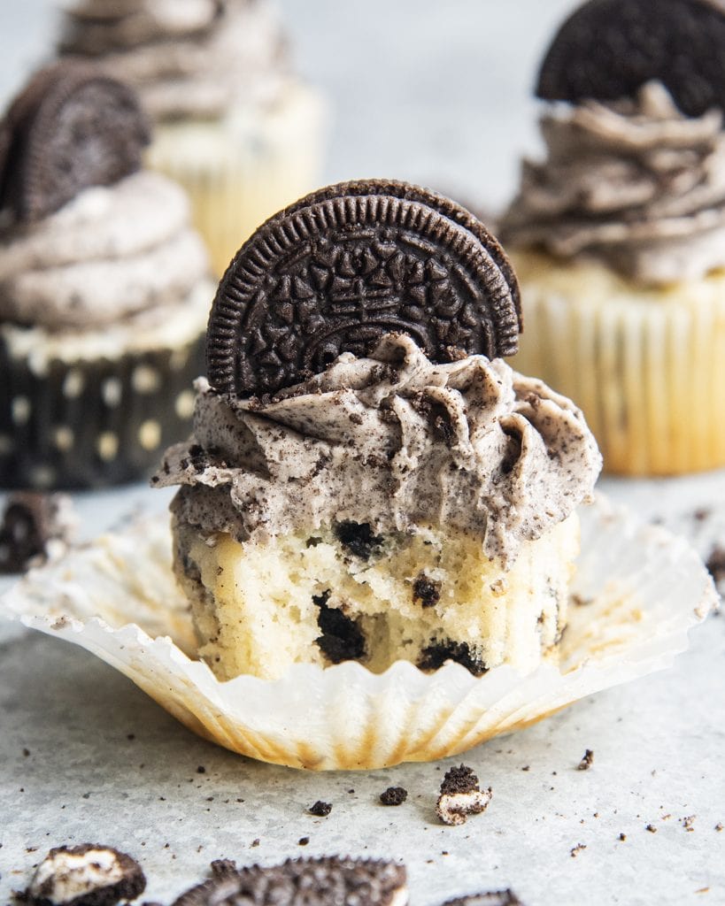 An overo cupcake on a cupcake liner with a bite taken out of it.