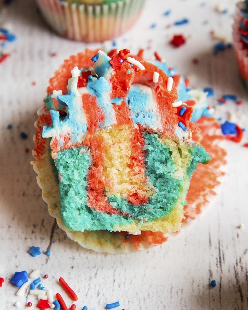 A red white and blue cupcake cut in half showing the middle of the cupcake, and red, white, and blue frosting on top.