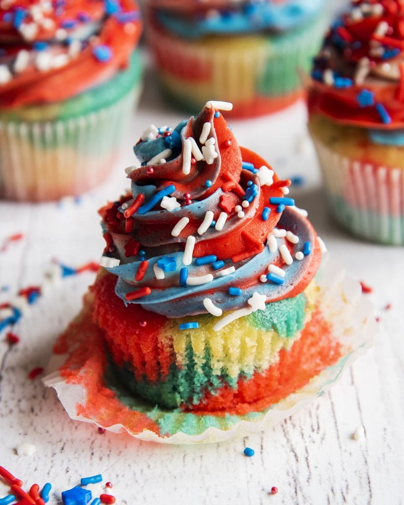 A red white and blue cupcake with the cupcake wrapper pulled off and sitting underneath it.