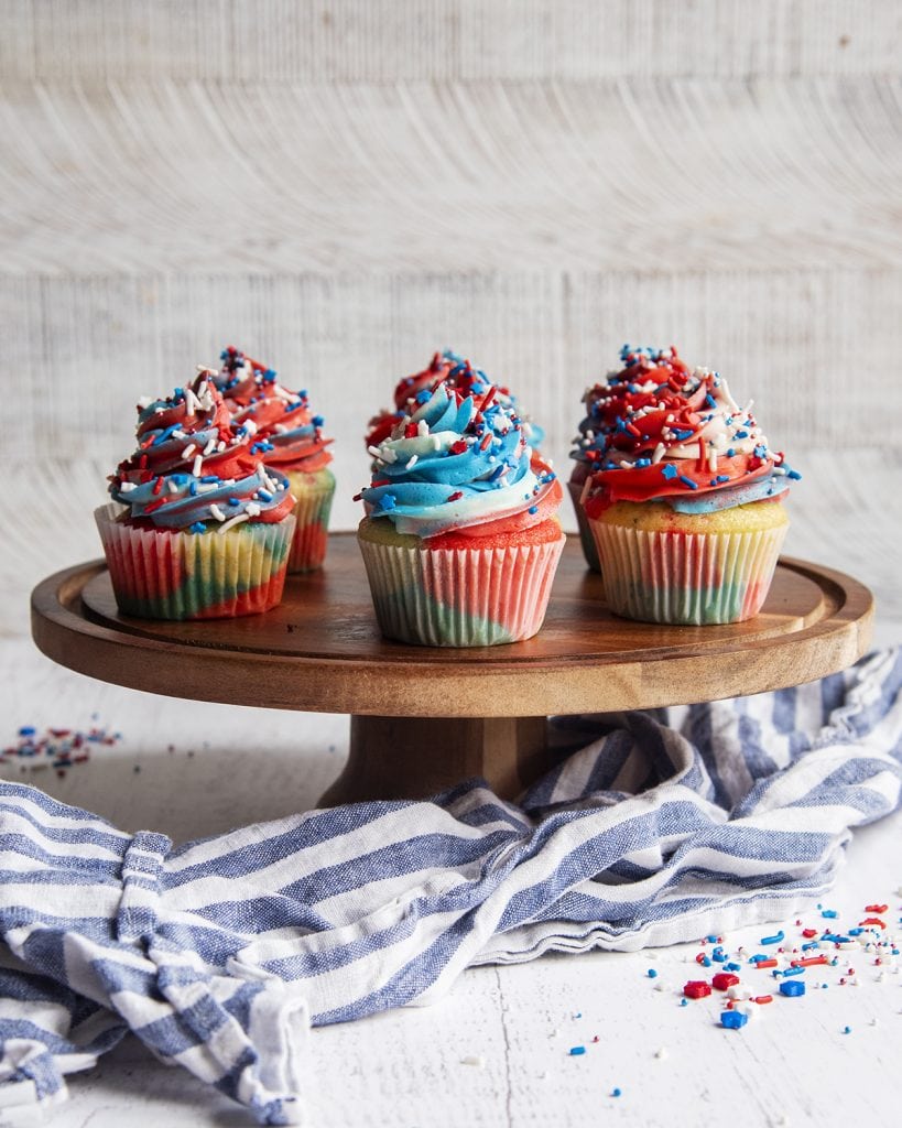 Red white and blue frosted fourth of July cupcakes on a wooden cake stand.