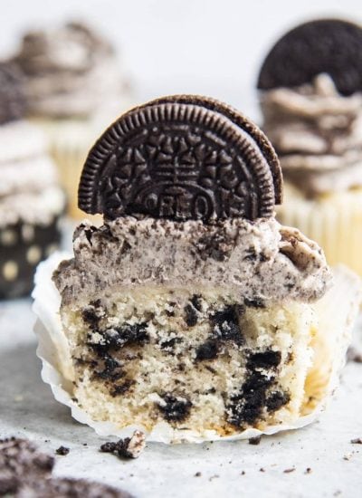 A frosted Oreo cupcake cut in half showing pieces of Oreos throughout the vanilla cupcake.