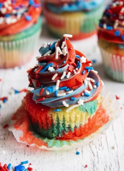 A red white and blue cupcake with the cupcake wrapper pulled off and sitting underneath it.