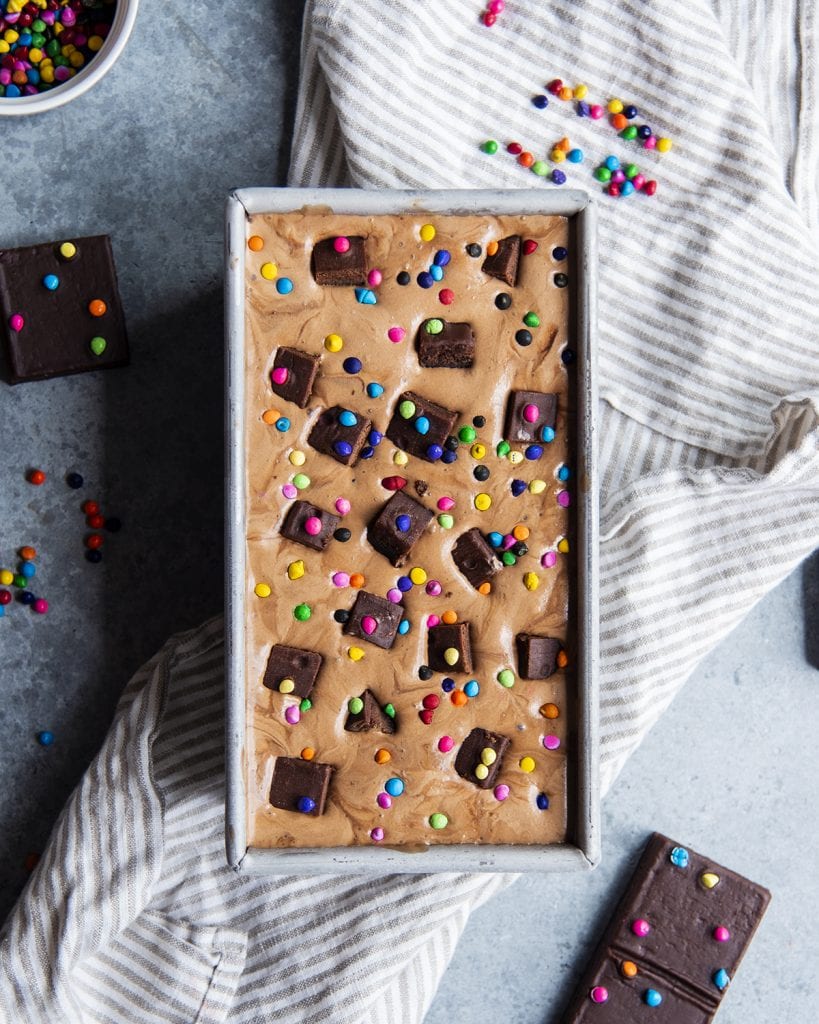 An overhead photo of a container of chocolate ice cream topped with pieces of cosmic brownies.