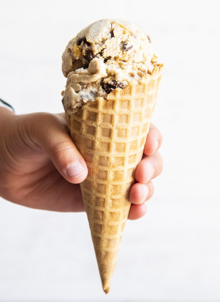 A child's hand holding an ice cream cone full of graham cracker ice cream.