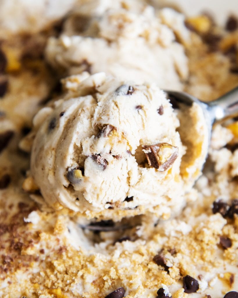 A close up of a scoop of graham cracker flavored ice cream with a graham cracker swirl, and chocolate honey comb candy pieces.