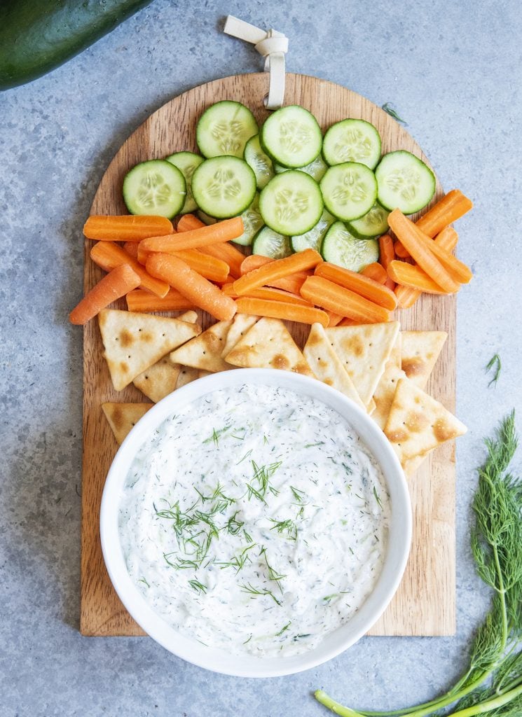 An overhead photo of a tray of vegetables and pita chips with a bowl of tzatziki sauce next to it.