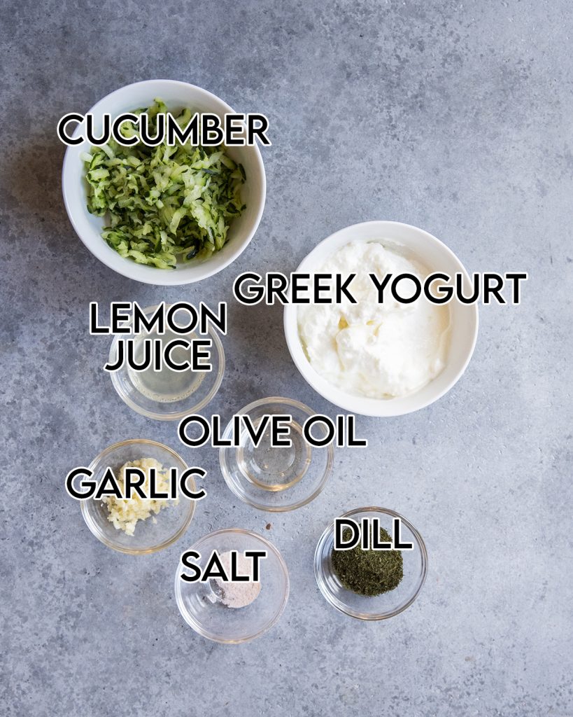 An overhead photo of the ingredients needed to make homemade tzatziki sauce, with text overlay labeling each ingredient.