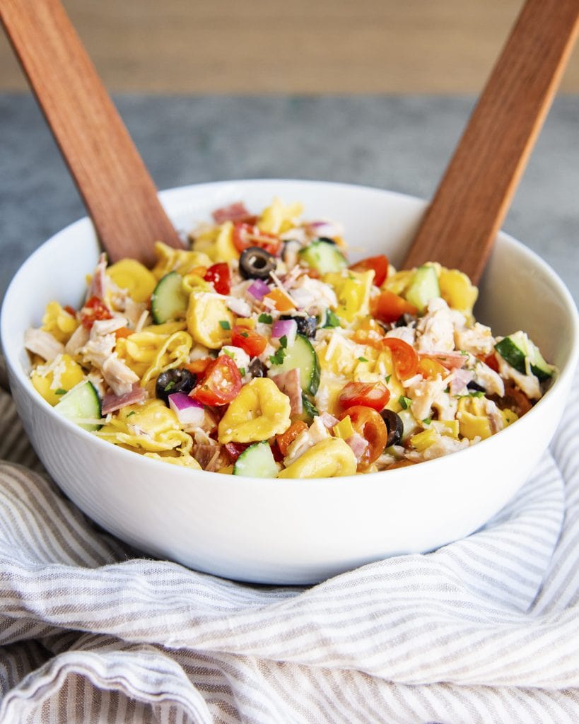 A bowl of tortellini pasta salad, loaded with shredded chicken, cucumbers, tomatoes, bell pepper, and tortellini.